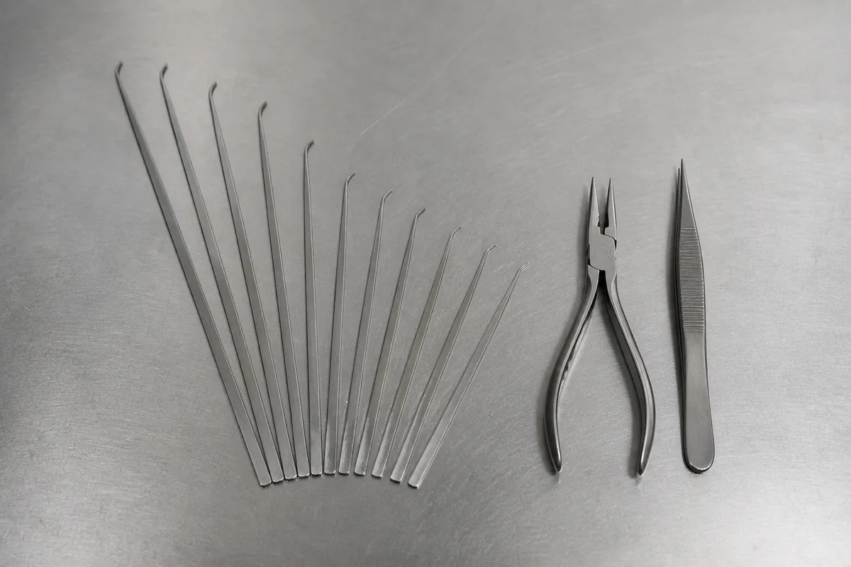 Jeu de lames d&rsquo;extracteur de clé cassée disposé à côté d&rsquo;une pince à becs fins sur un plan de travail d&rsquo;atelier