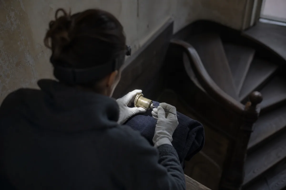 Technicien manipulant un cylindre de serrure à la lampe frontale sur une porte d&rsquo;immeuble ancien, mains gantées, sans visage visible