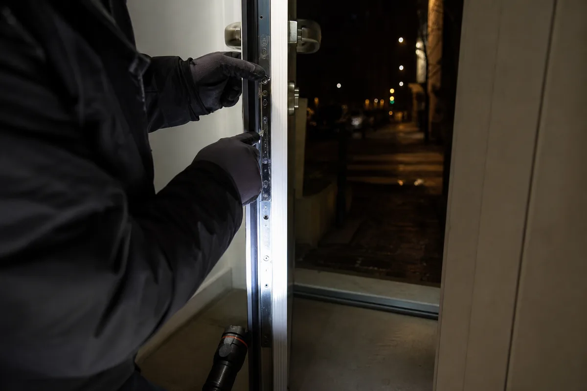 Mains d’un serrurier réglant une serrure multipoint sur une porte, éclairage nocturne contrasté